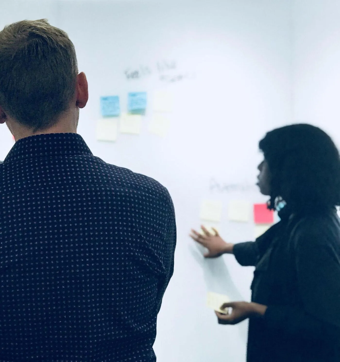 Two people at a whiteboard covered in sticky notes, softly out of focus.